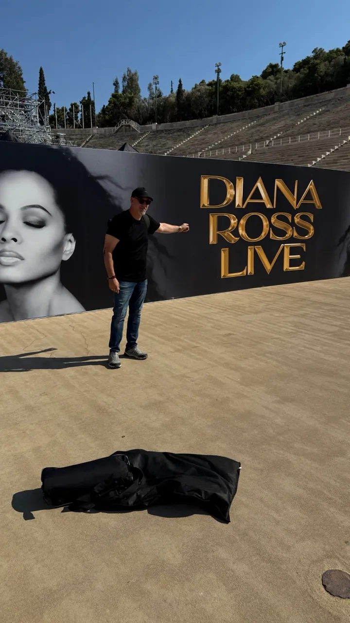 John standing in an ancient stadium in front of a Diana Ross Live banner.