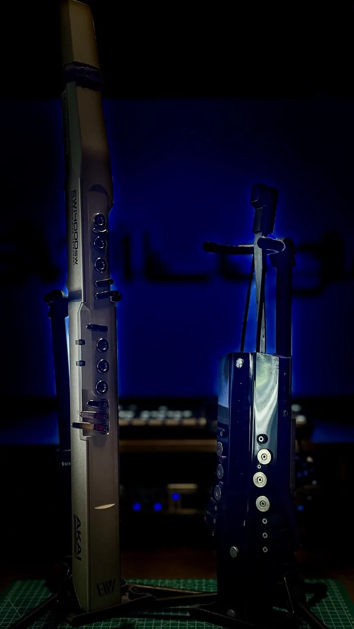 A silver EWI and the dark Nurad unit on stands in blue light.