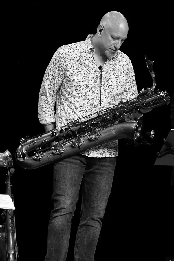 Black-and-white photo of John looking down at a baritone saxophone.