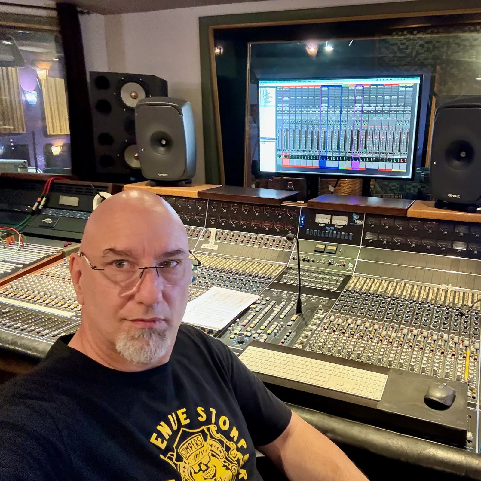 John at the large mixing console in the control room, studio monitors and a screen of Logic Pro behind him.