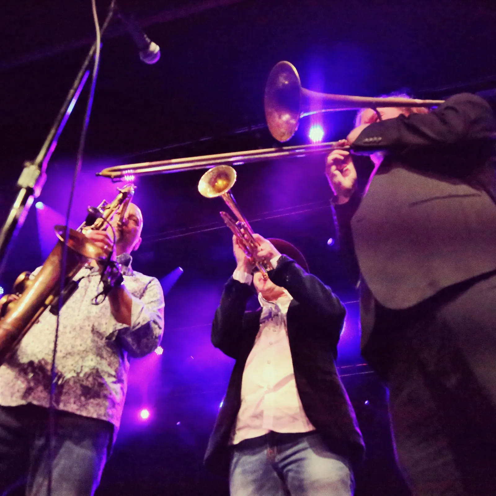 Saxophone, trumpet and trombone players in purple stage light.