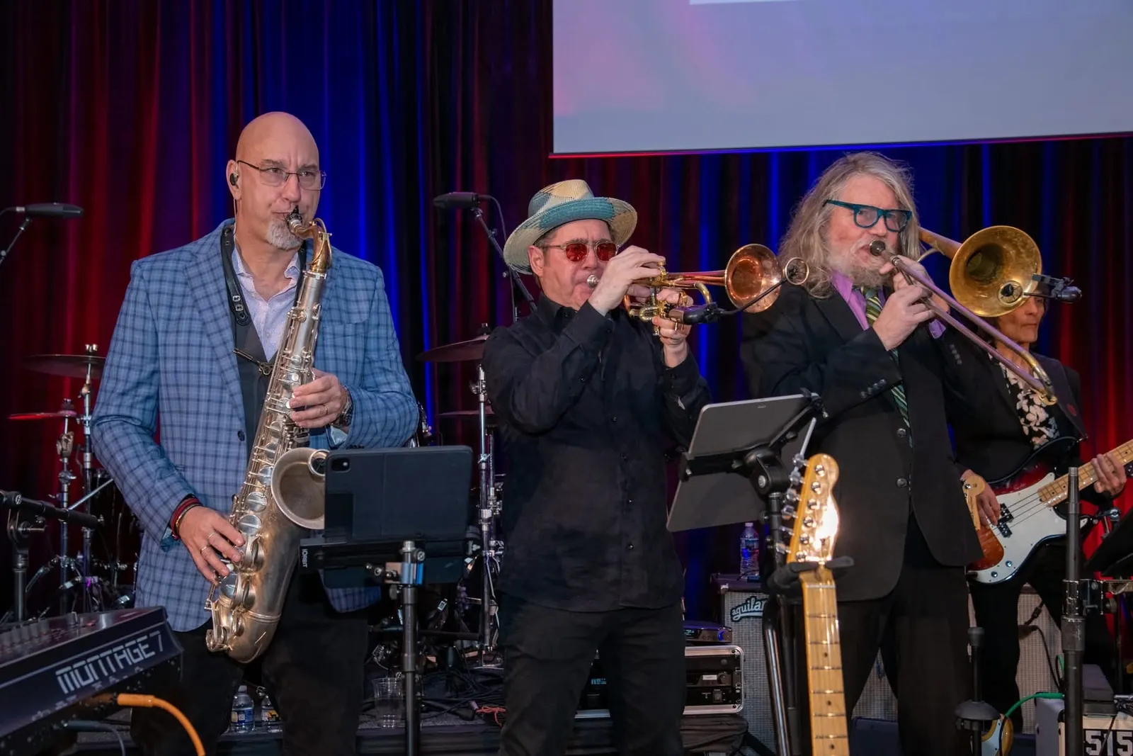 John on tenor saxophone with a trumpet and a trombone player on a stage.