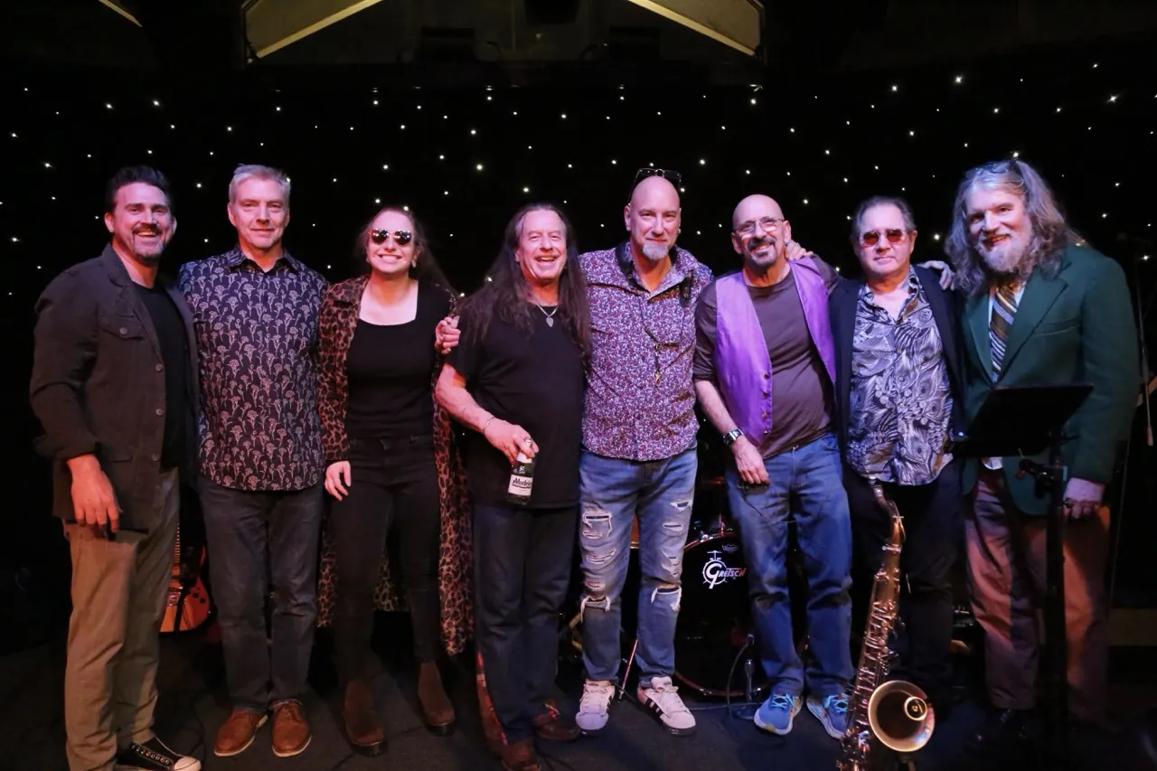 John and eight bandmates posing on a starry stage.