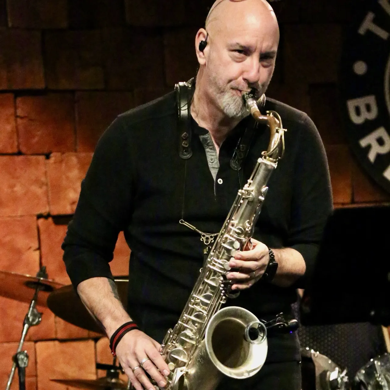 John playing tenor saxophone on stage in front of a brick wall.