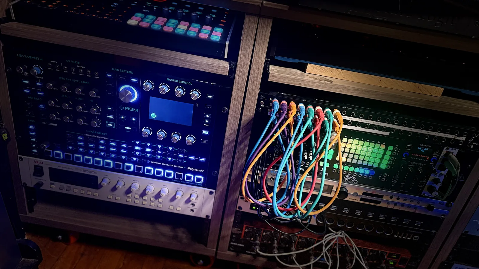 A rack of synthesizers and processors with colored patch cables in the studio.